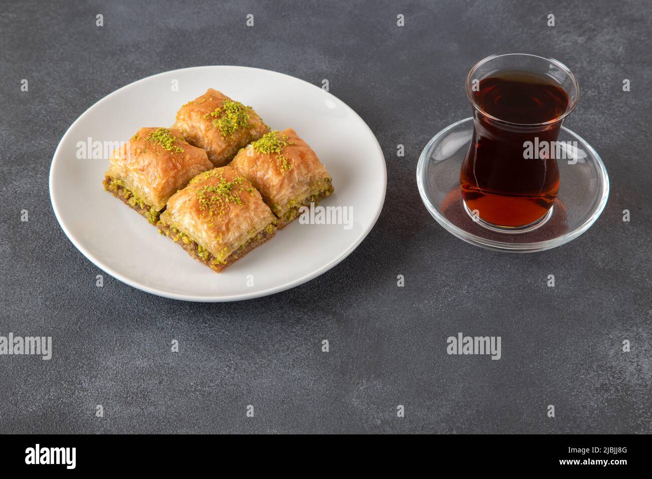 Plaque de baklava traditionnelle à la pistache avec du thé turc. Plaque de baklava sur fond sombre Banque D'Images