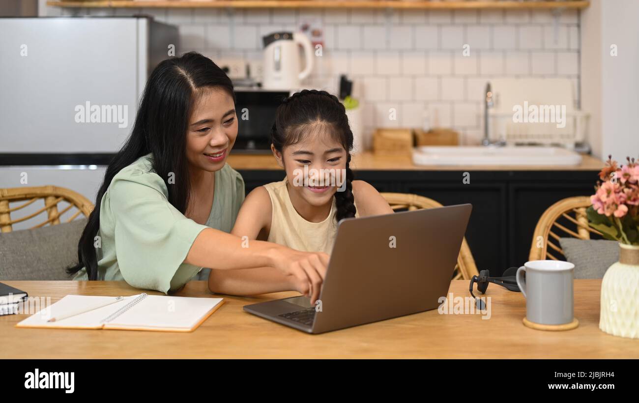 Souriant petite fille asiatique d'apprentissage Internet classe en ligne et de faire des devoirs avec sa mère dans la cuisine. Concept d'éducation à l'apprentissage en ligne Banque D'Images