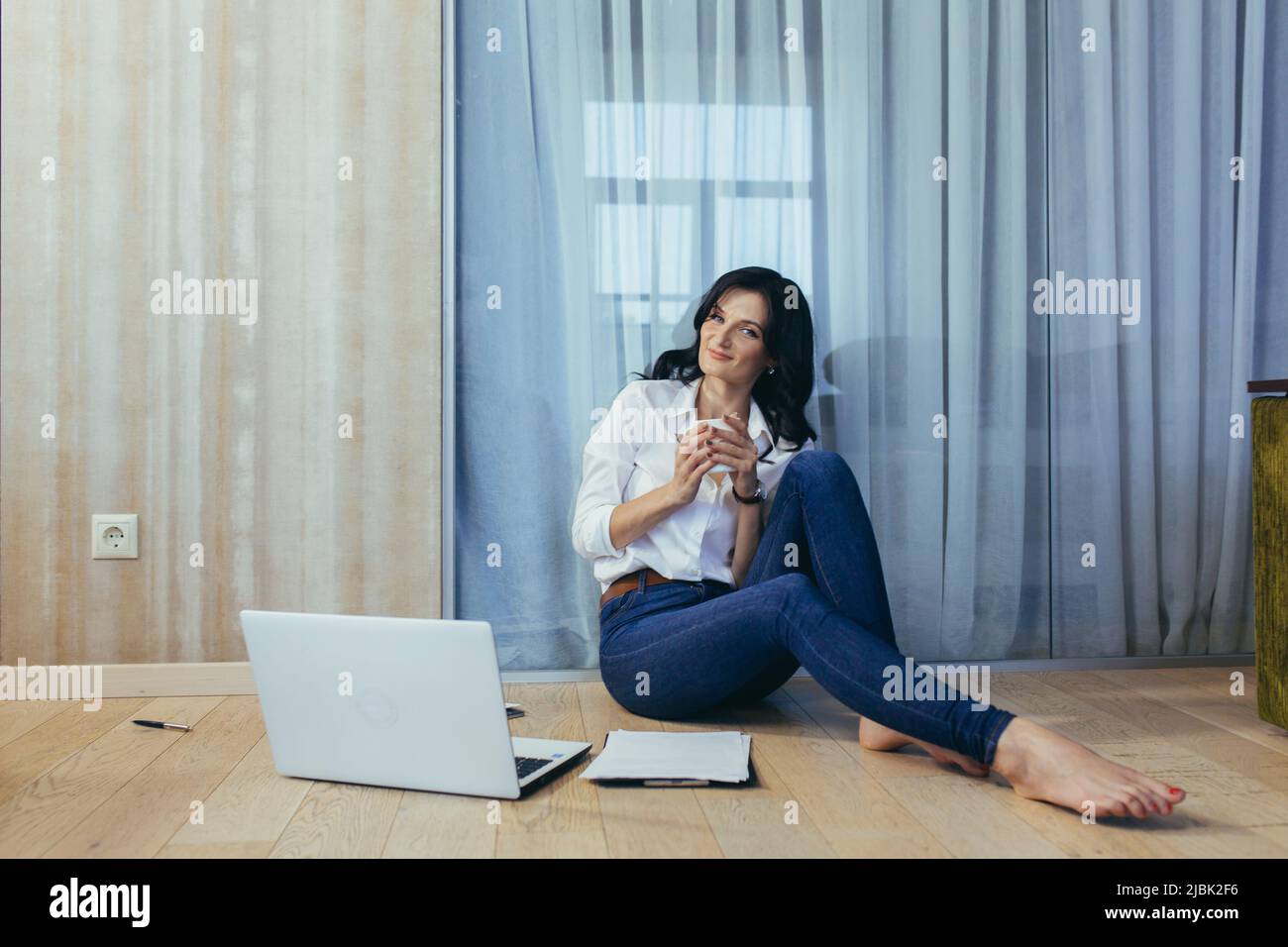 Belle jeune femme travaillant, faisant des affaires, étudiant à la maison en ligne, parlant au téléphone, sur la vidéo, assis sur le sol dans la chambre, faisant du papier Banque D'Images