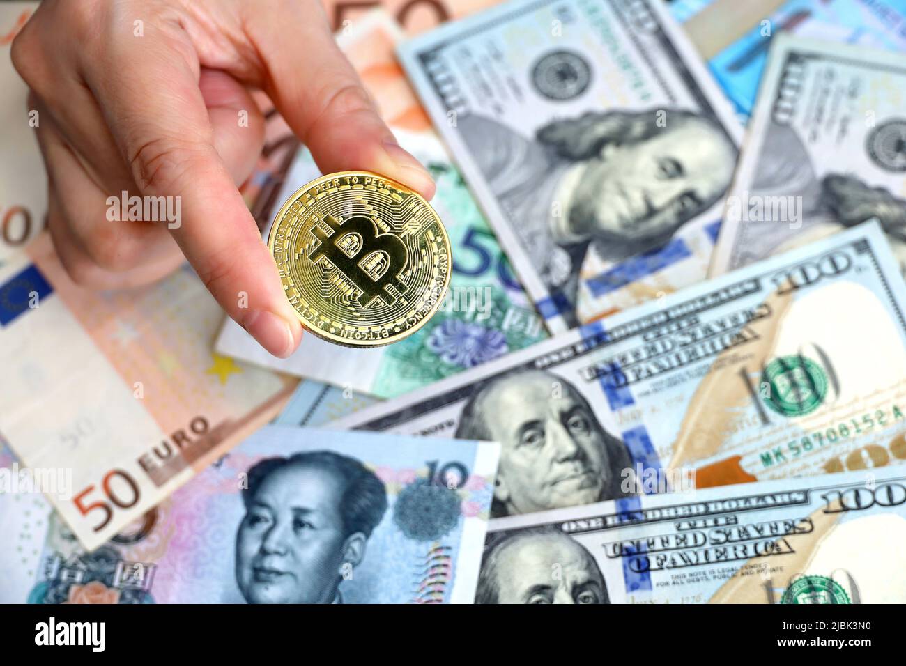 Bitcoin en main féminine sur fond de billets en dollars américains, en euros et en yuans. Monnaie électronique décentralisée, taux de change Banque D'Images