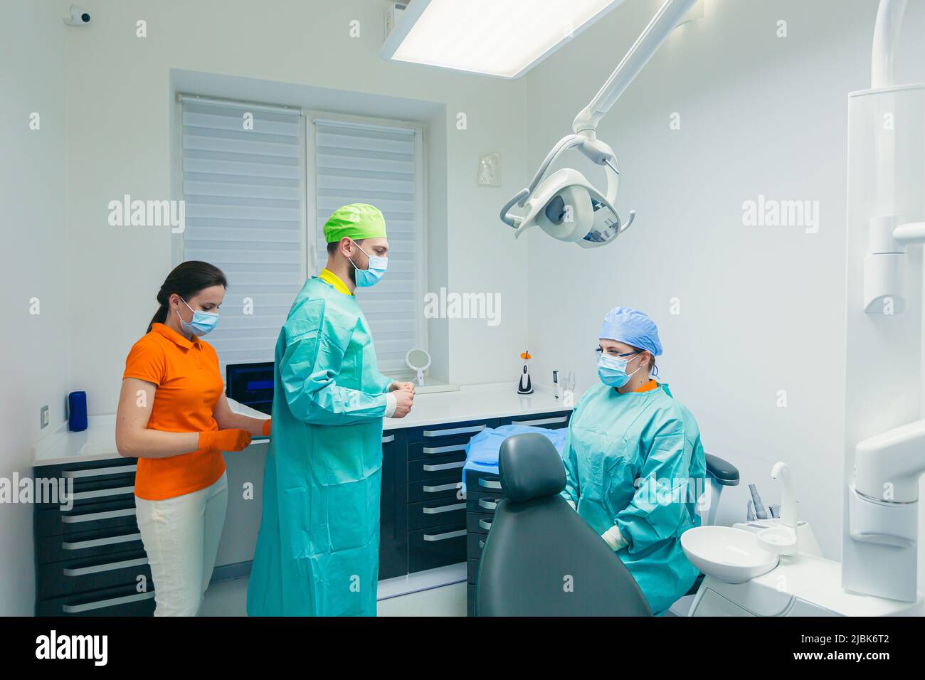 Jeune femme médecin assistant aide le dentiste à se préparer pour le traitement, la chirurgie, met sur le peignoir, l'uniforme dans le bureau Banque D'Images