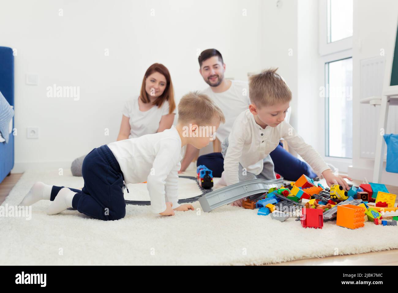 Jeune famille, maman, papa, deux enfants, à la maison dans une chambre sur le sol jouant avec un chemin de fer jouet, un designer, s'amuser. Rire Banque D'Images