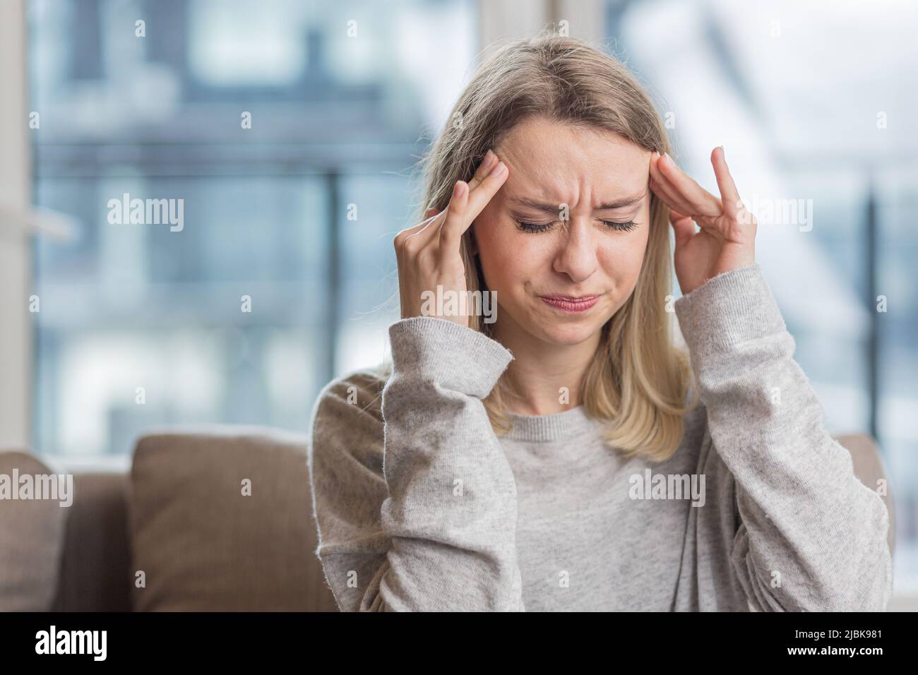 La jeune femme a un mal de tête, tient sa tête avec ses mains et fait des douleurs à la maison, au bureau au travail Banque D'Images