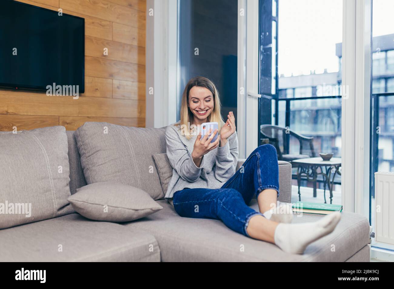 Bonne belle jeune femme assise sur un canapé à la maison regardant le téléphone et heureux de gagner un prix, appris de bonnes nouvelles, message Banque D'Images