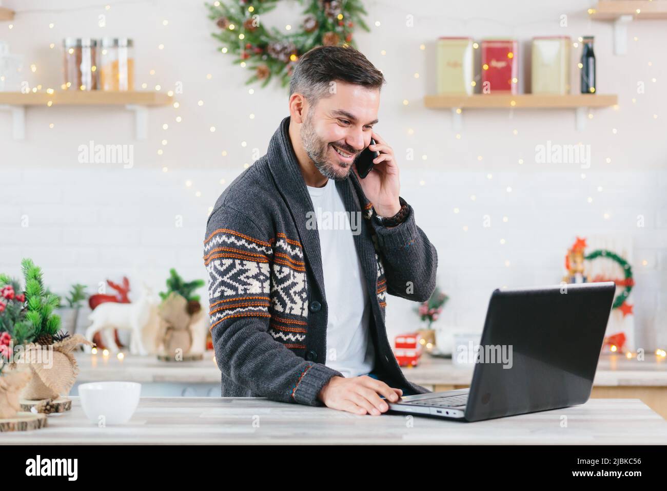 Un entrepreneur indépendant heureux et réussi travaillant sur un ordinateur portable à la maison parlant au téléphone pendant les fêtes du nouvel an termine le projet par deadl Banque D'Images