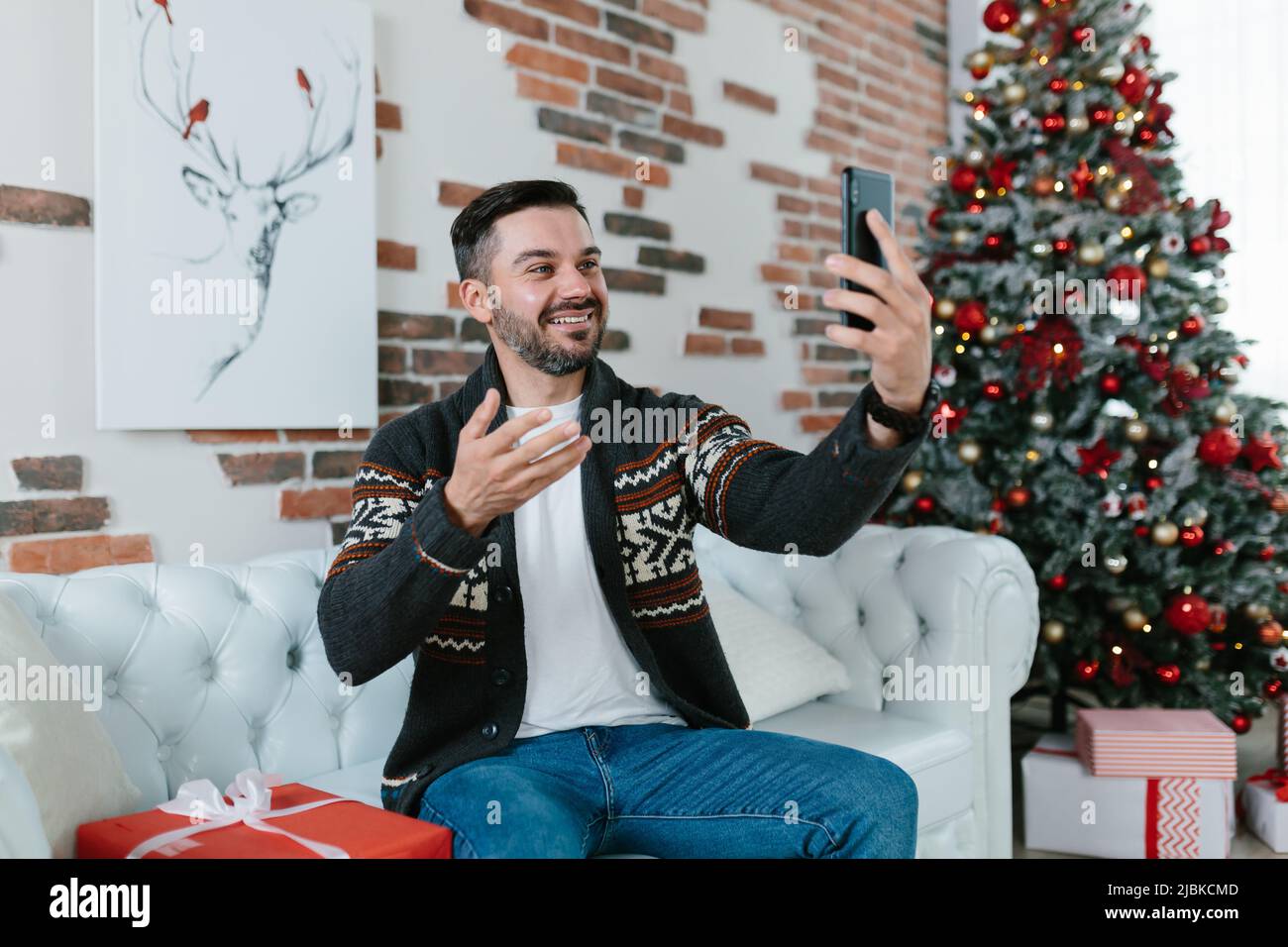 L'homme lui-même célèbre Noël à la maison, reçoit les salutations de ses amis communique par vidéo en utilisant l'application sur le téléphone Banque D'Images