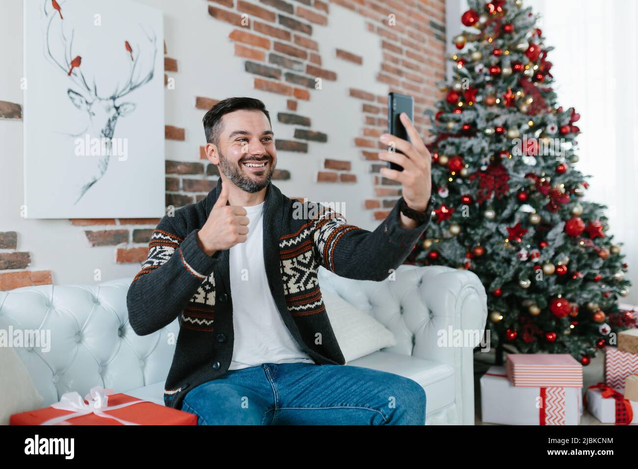 L'homme lui-même célèbre Noël à la maison, reçoit les salutations de ses amis communique par vidéo en utilisant l'application sur le téléphone Banque D'Images