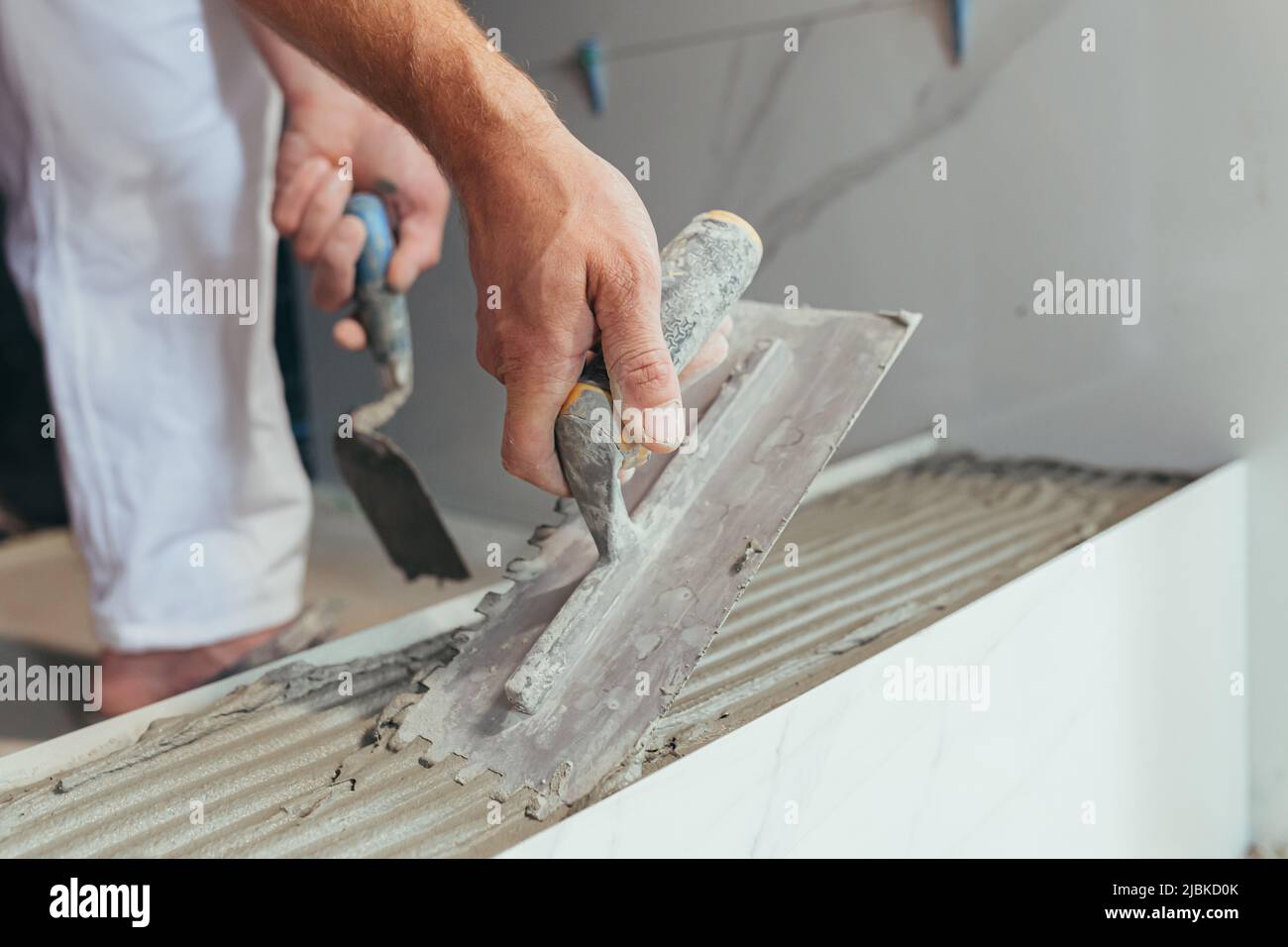 Homme ouvrier professionnel monte le carrelage en céramique dans la salle de bains photo avec une spatule fermée avec de la colle Banque D'Images