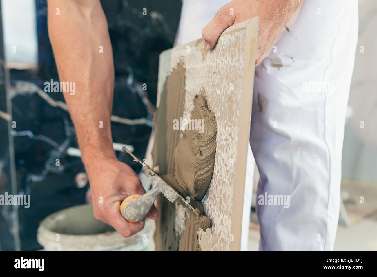 Homme ouvrier professionnel monte le carrelage en céramique dans la salle de bains photo avec une spatule fermée avec de la colle Banque D'Images