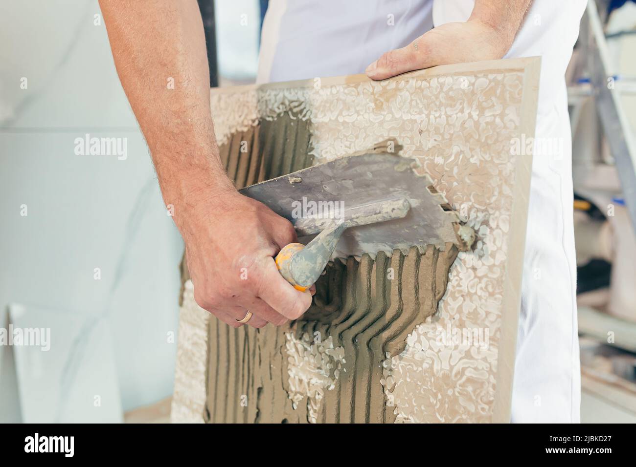 Homme ouvrier professionnel monte le carrelage en céramique dans la salle de bains photo avec une spatule fermée avec de la colle Banque D'Images