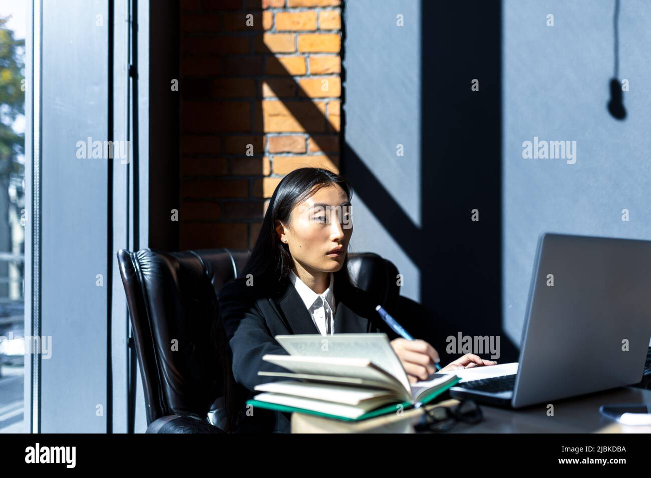 Jeune femme d'affaires asiatique indépendante travaillant dans un restaurant sur un ordinateur portable et confiante en regardant la caméra dans un costume d'affaires Banque D'Images