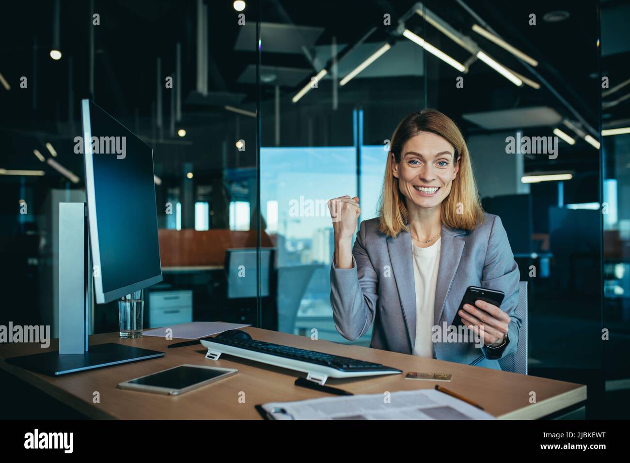 Femme d'affaires travaillant à un ordinateur dans un bureau moderne, le patron comptable se réjouit du rapport financier soumis, regarde la caméra et nous sourit Banque D'Images