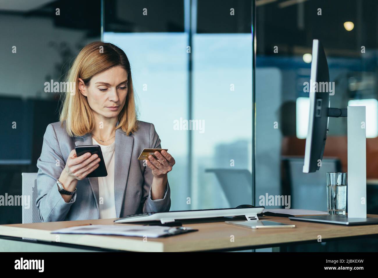 Une femme de banque d'affaires sérieuse effectue des opérations bancaires avec une carte de crédit et une application au téléphone, travaille dans un bureau de banque moderne Banque D'Images