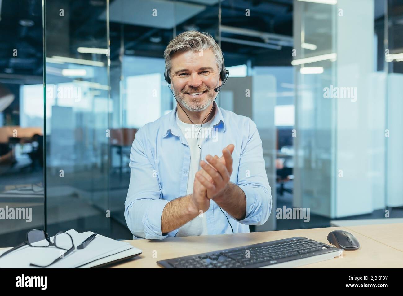 Un Manager expérimenté regarde la caméra et sourit, un homme d'affaires passe la main lors d'un appel vidéo, comme un signe de louange et de soutien aux interlocuteurs Banque D'Images