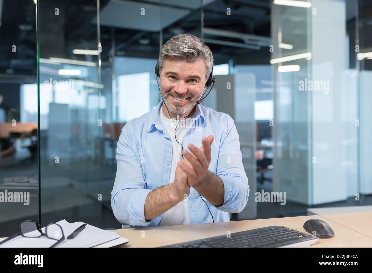 Un Manager expérimenté regarde la caméra et sourit, un homme d'affaires passe la main lors d'un appel vidéo, comme un signe de louange et de soutien aux interlocuteurs Banque D'Images