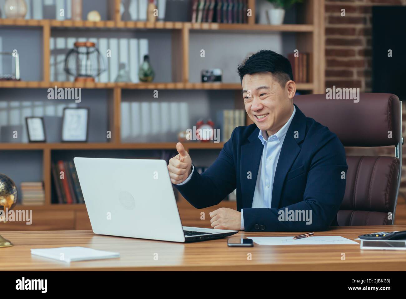 Jeune homme d'asie beau, homme d'affaires, avocat, directeur parlant sur un appel vidéo à partir d'un ordinateur portable dans le bureau, tient une réunion, consultation, discussion Banque D'Images