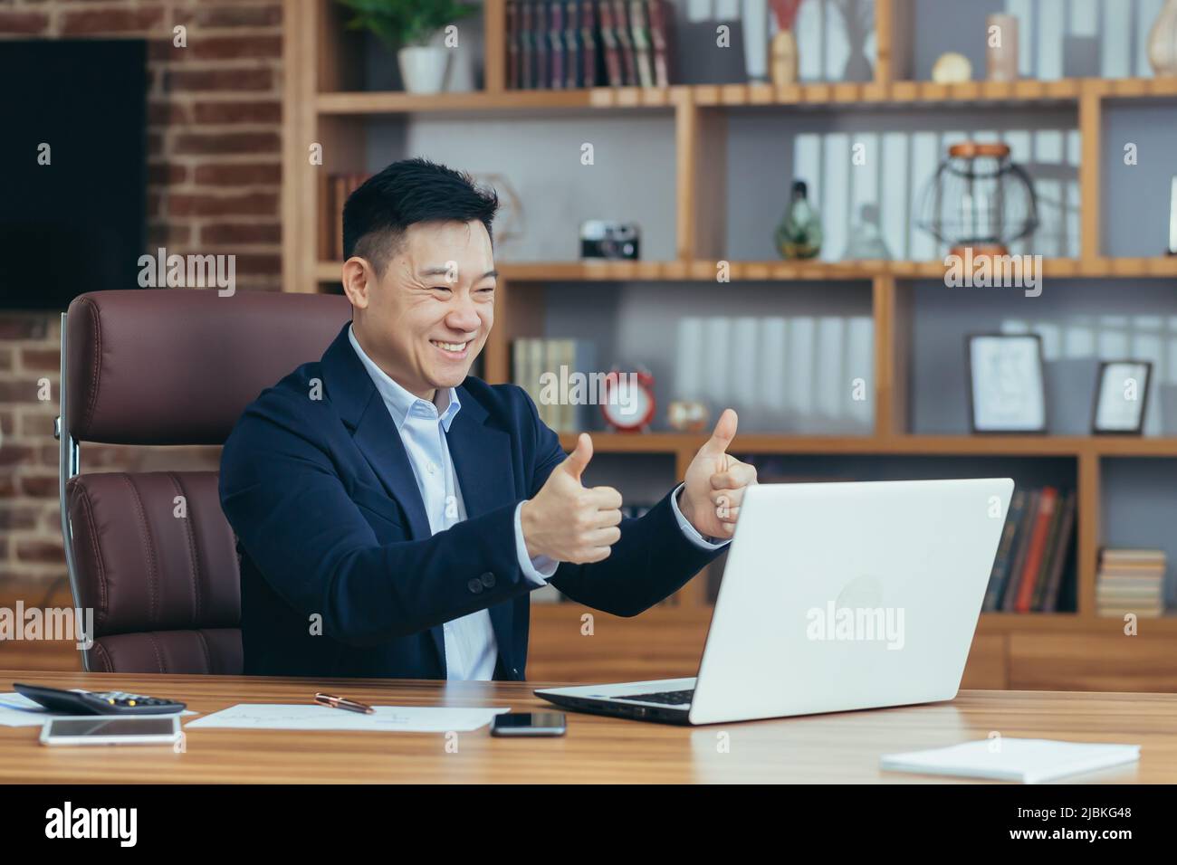 Jeune homme d'asie beau, homme d'affaires, avocat, directeur parlant sur un appel vidéo à partir d'un ordinateur portable dans le bureau, tient une réunion, consultation, discussion Banque D'Images