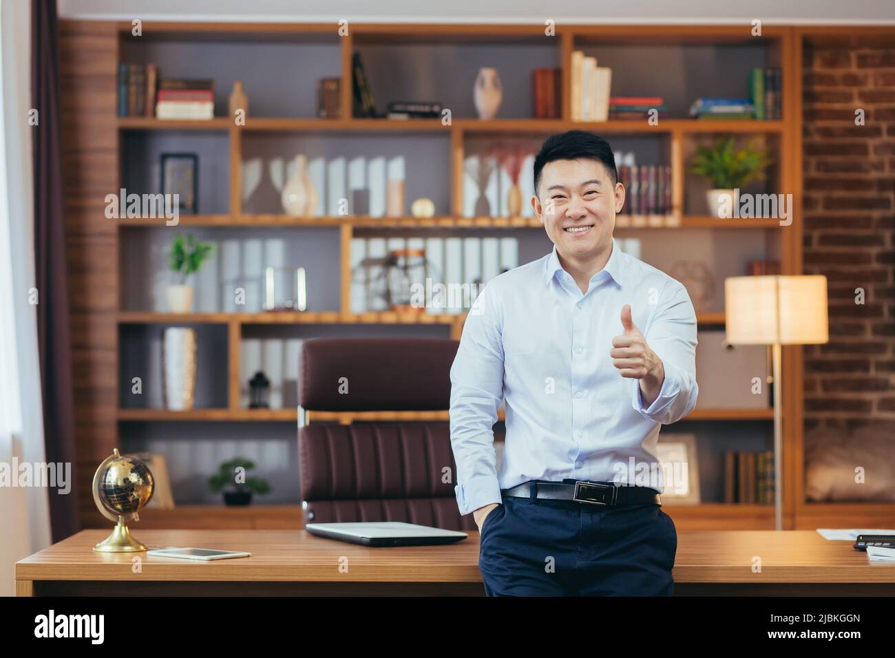 Portrait d'un directeur d'université réussi, un professeur asiatique en chemise regarde l'appareil photo et sourit, garde son doigt vers le haut, encourage les jeunes Banque D'Images