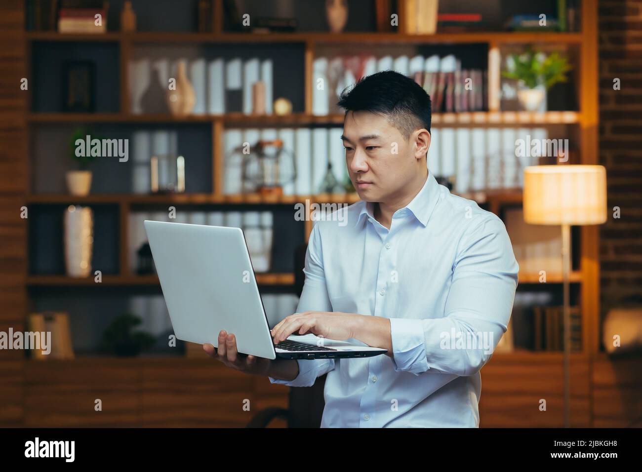 Homme d'affaires sérieux travaillant sur un ordinateur portable, asiatique regardant l'écran, focalisé la lecture et la recherche de données économiques Banque D'Images