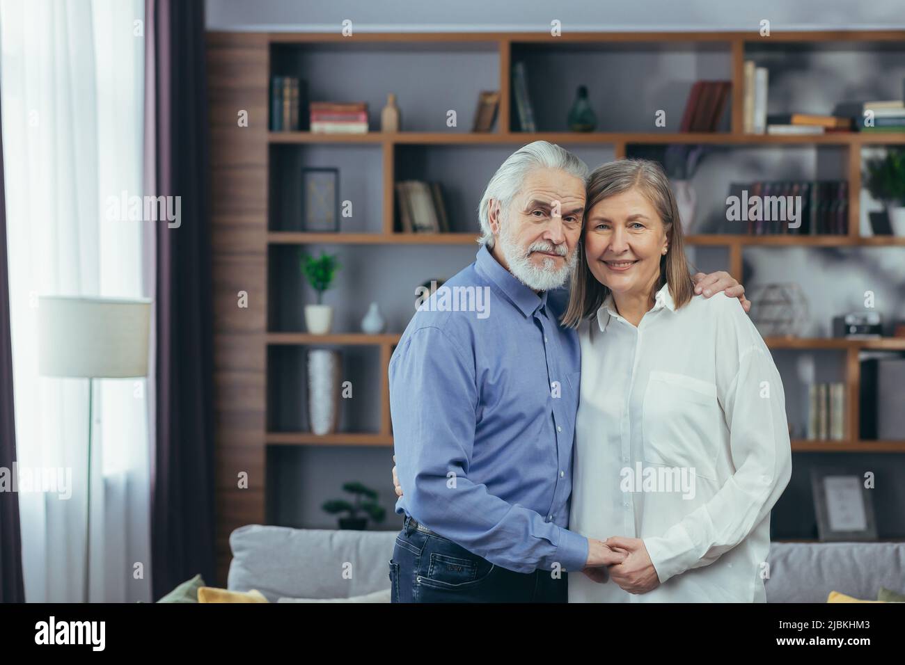 Heureux couple marié, homme et femme aux cheveux gris, souriant et regardant l'appareil photo, enserrant le portrait à la maison Banque D'Images