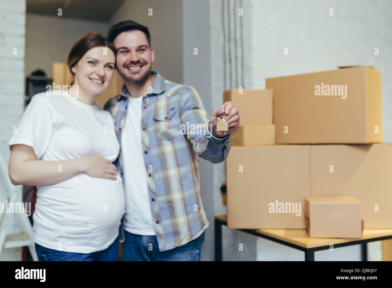 Jeune famille heureuse s'attendant à un bébé. Femme enceinte et mari ont déménagé dans une nouvelle maison, appartement. Déballer les boîtes avec les objets. Enserrer, sourire Banque D'Images