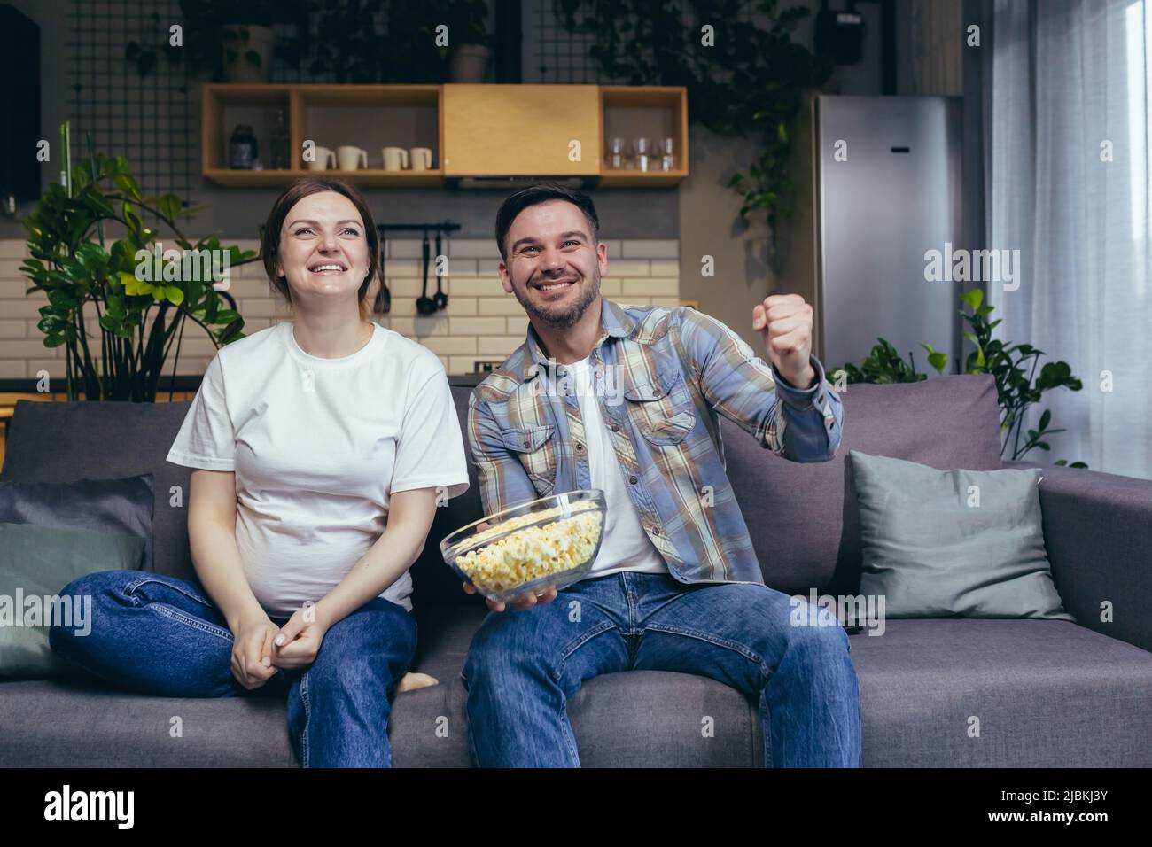 Couple marié homme et femme enceinte ensemble sur le canapé ensemble regardant les matchs de sport acclamations et de manger du pop-corn Banque D'Images