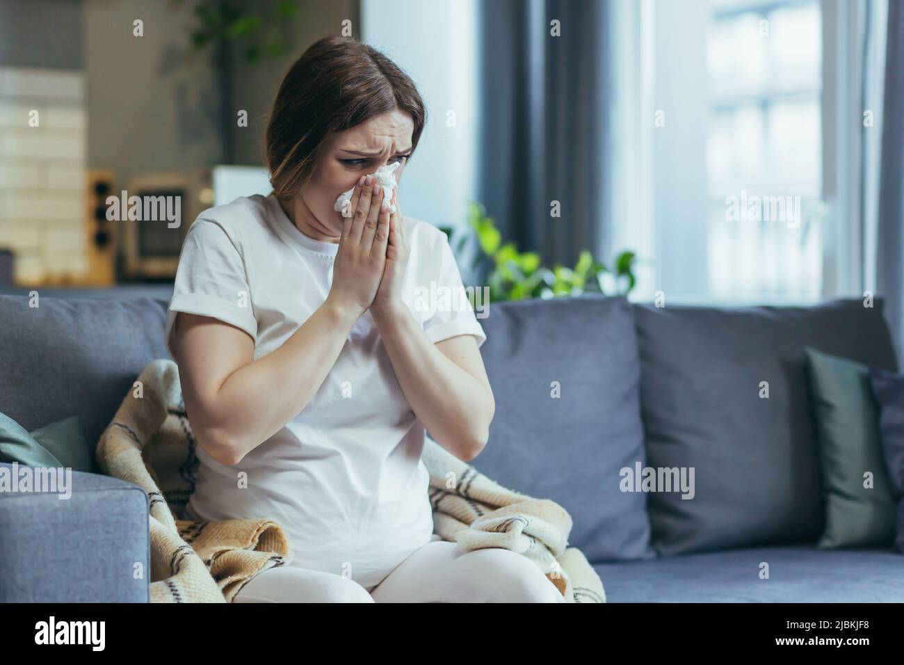 Triste femme enceinte à la maison assise sur le canapé et pleurant, a un nez qui coule et des allergies éternuent dans une serviette Banque D'Images