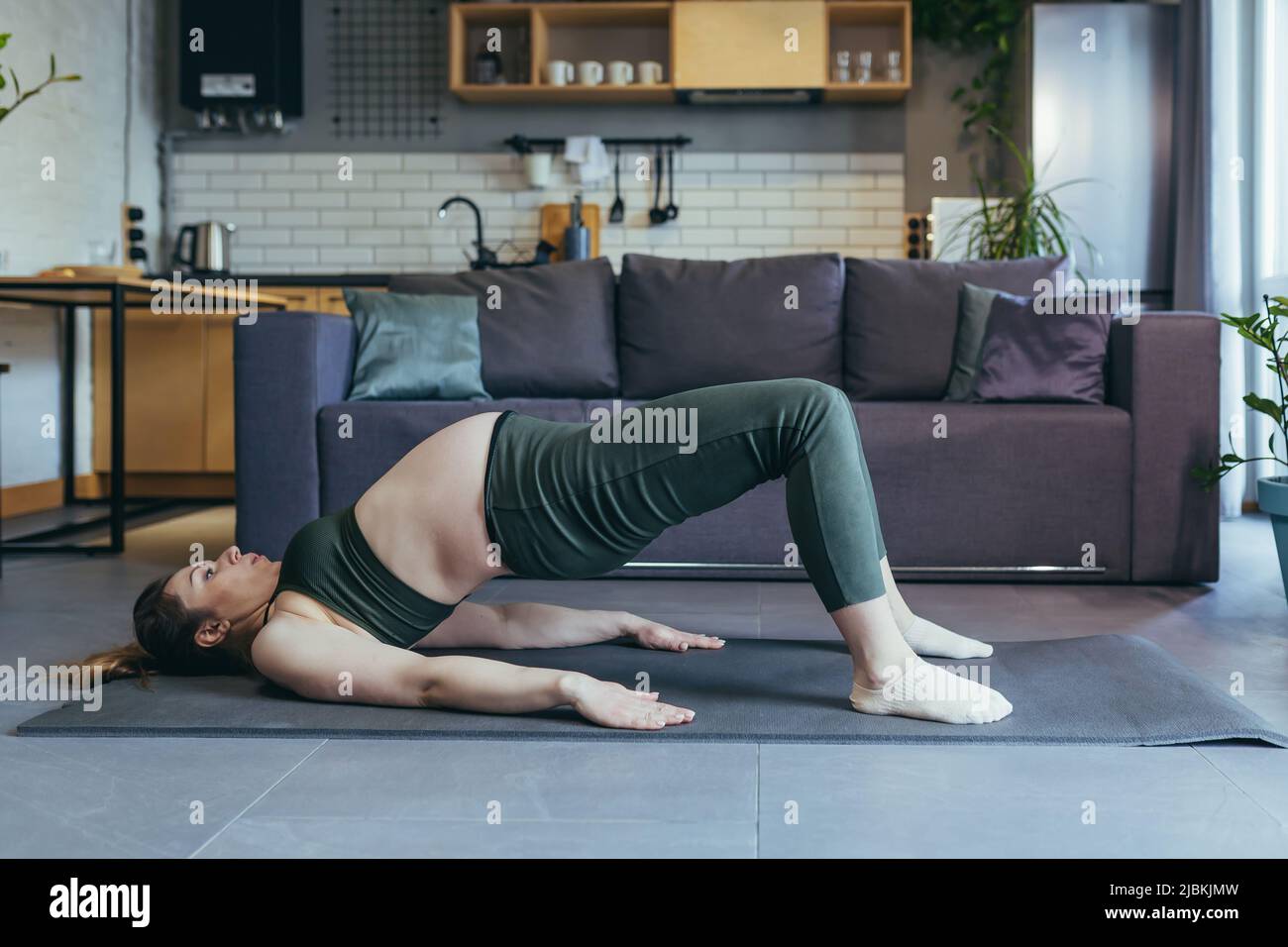 Femme enceinte belle va pour le sport à la maison, s'assoit et se repose sur un tapis de sport dans un uniforme de sport, fait des exercices, est satisfait Banque D'Images