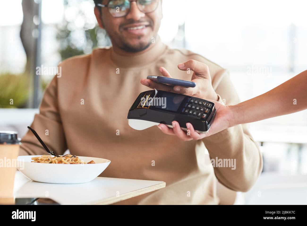 Gros plan de jeune homme payant avec smartphone NFC dans un café à l'aire de restauration, espace de copie Banque D'Images