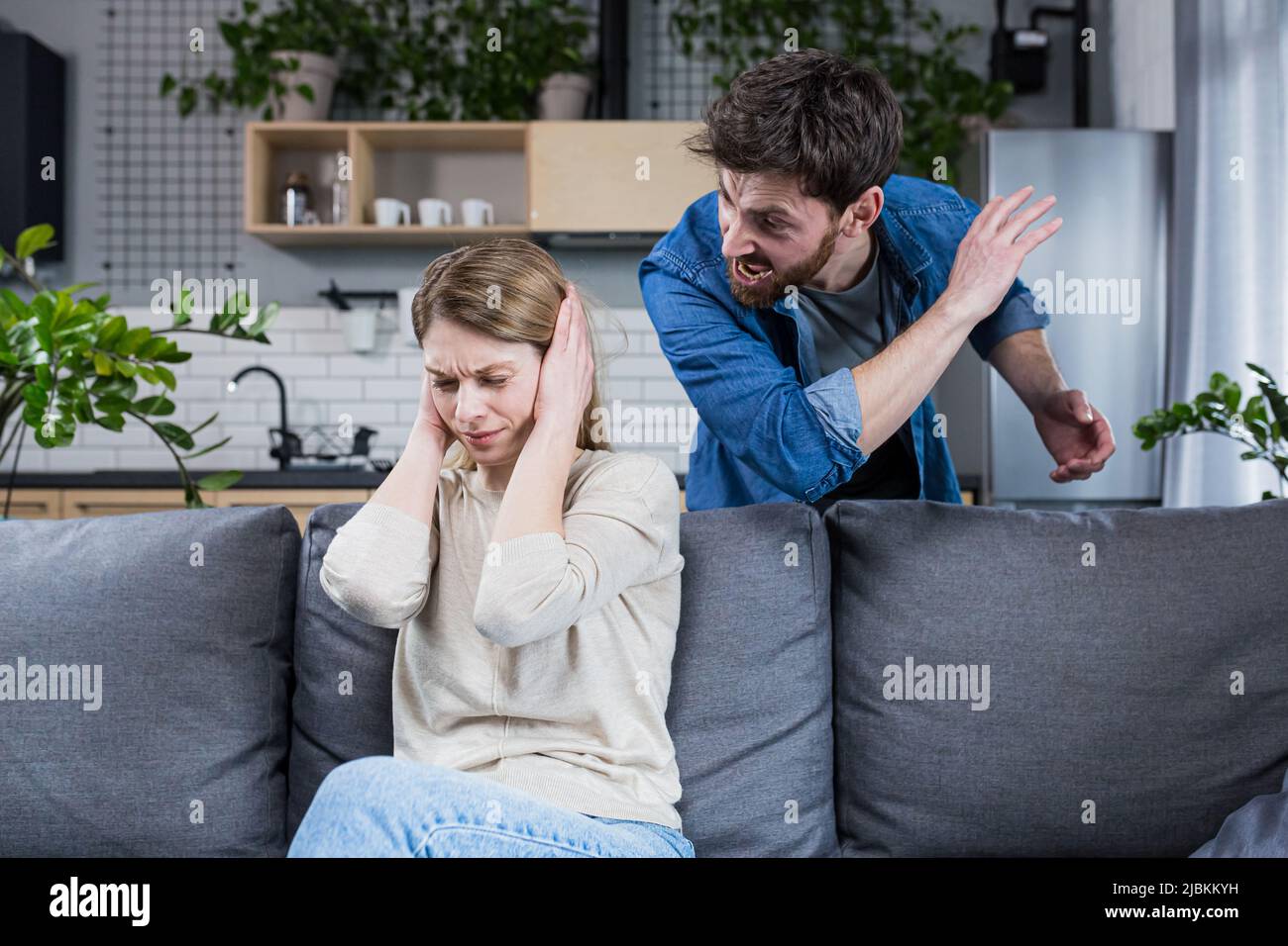 Violence domestique. Conflit familial. Un homme crie chez une femme à la maison. La femme a fermé ses oreilles. Assis sur le canapé. Banque D'Images