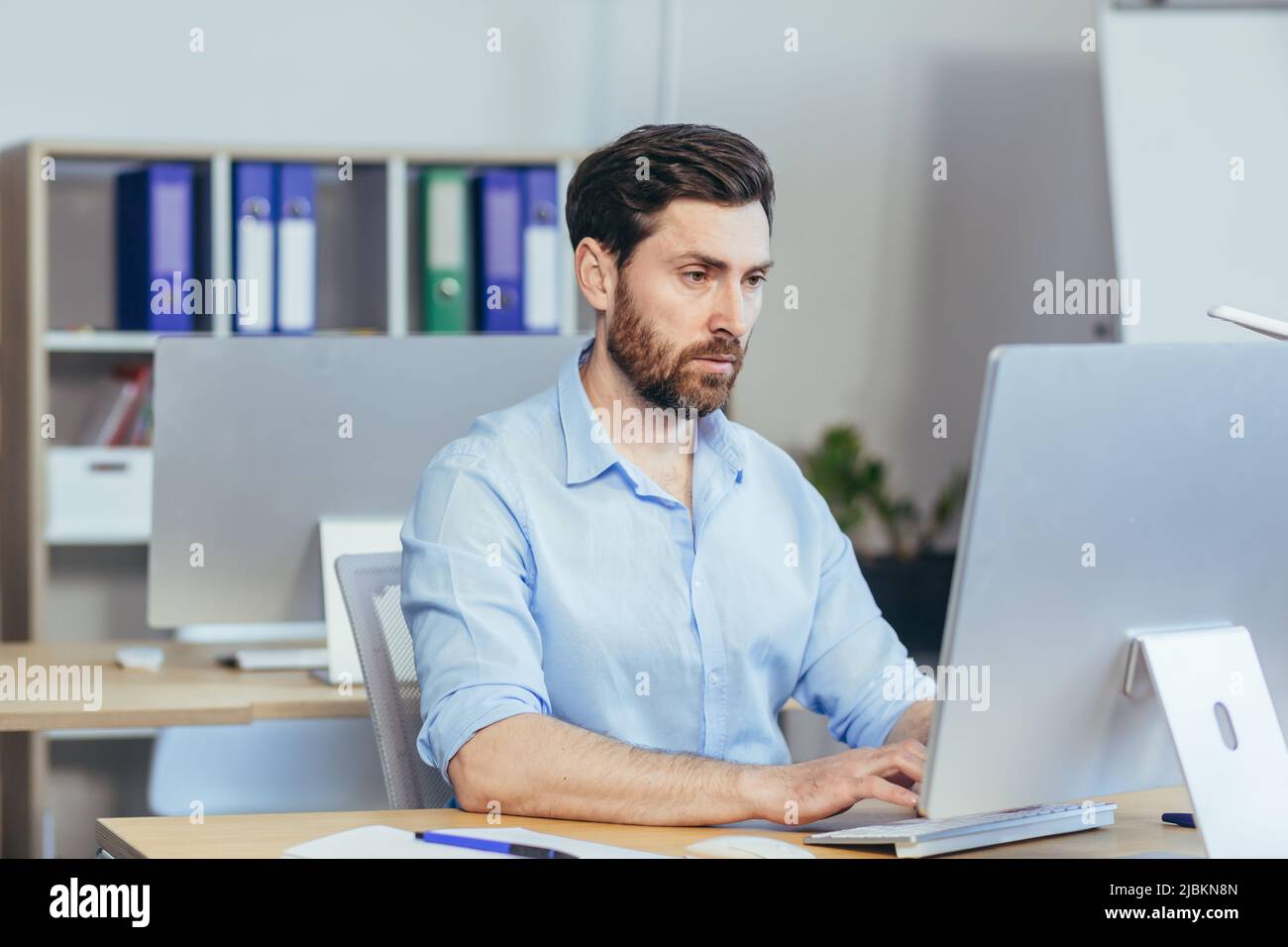 Portrait d'un homme d'affaires sérieux et concentré, un homme travaillant dans un bureau lumineux pendant la journée, à l'ordinateur regardant le moniteur, dans un caillot occasionnel Banque D'Images