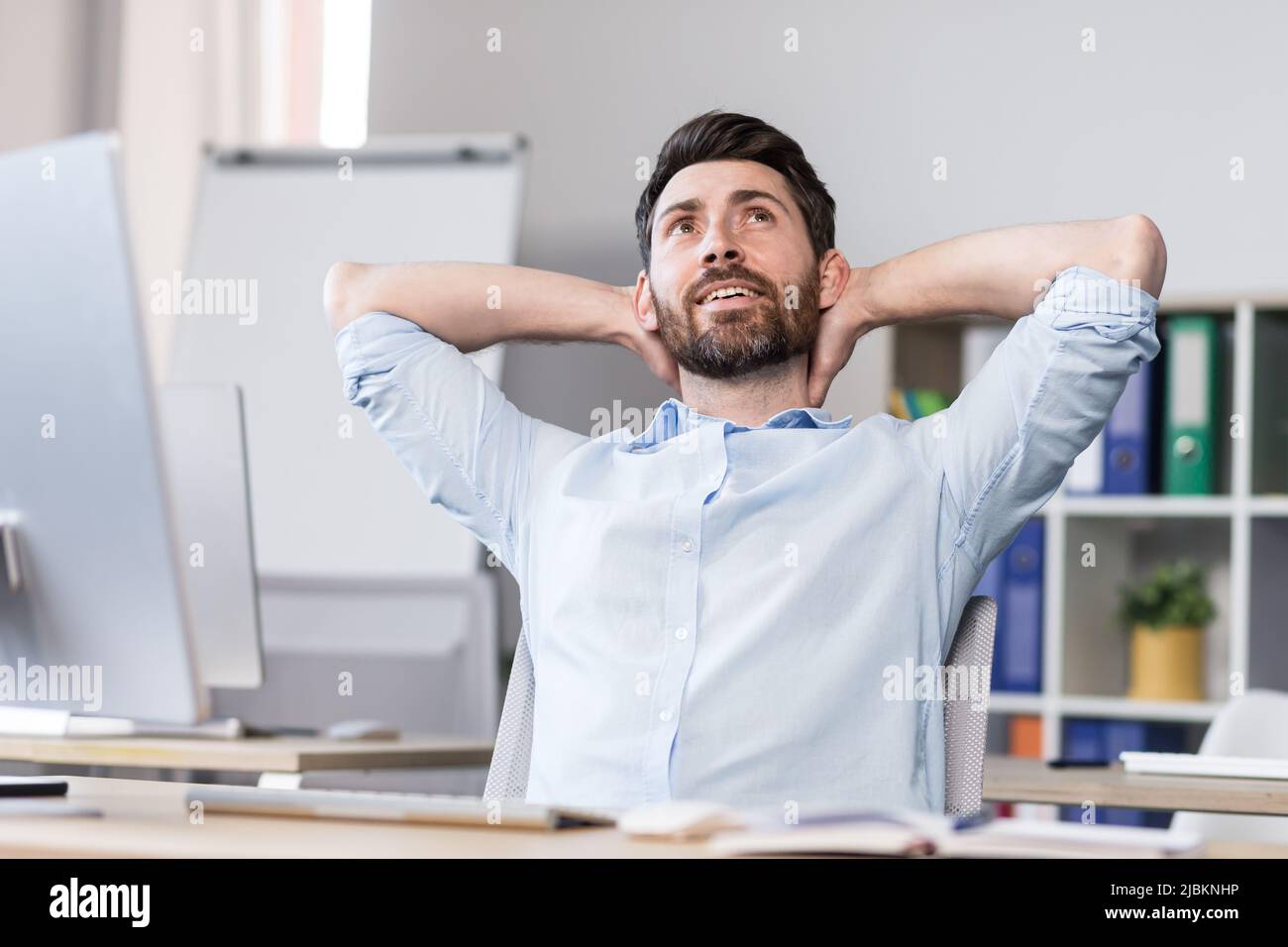 Homme d'affaires au bureau se reposant de façon rêveuse, jetant les mains derrière sa tête, homme travaillant sur un projet d'entreprise Banque D'Images