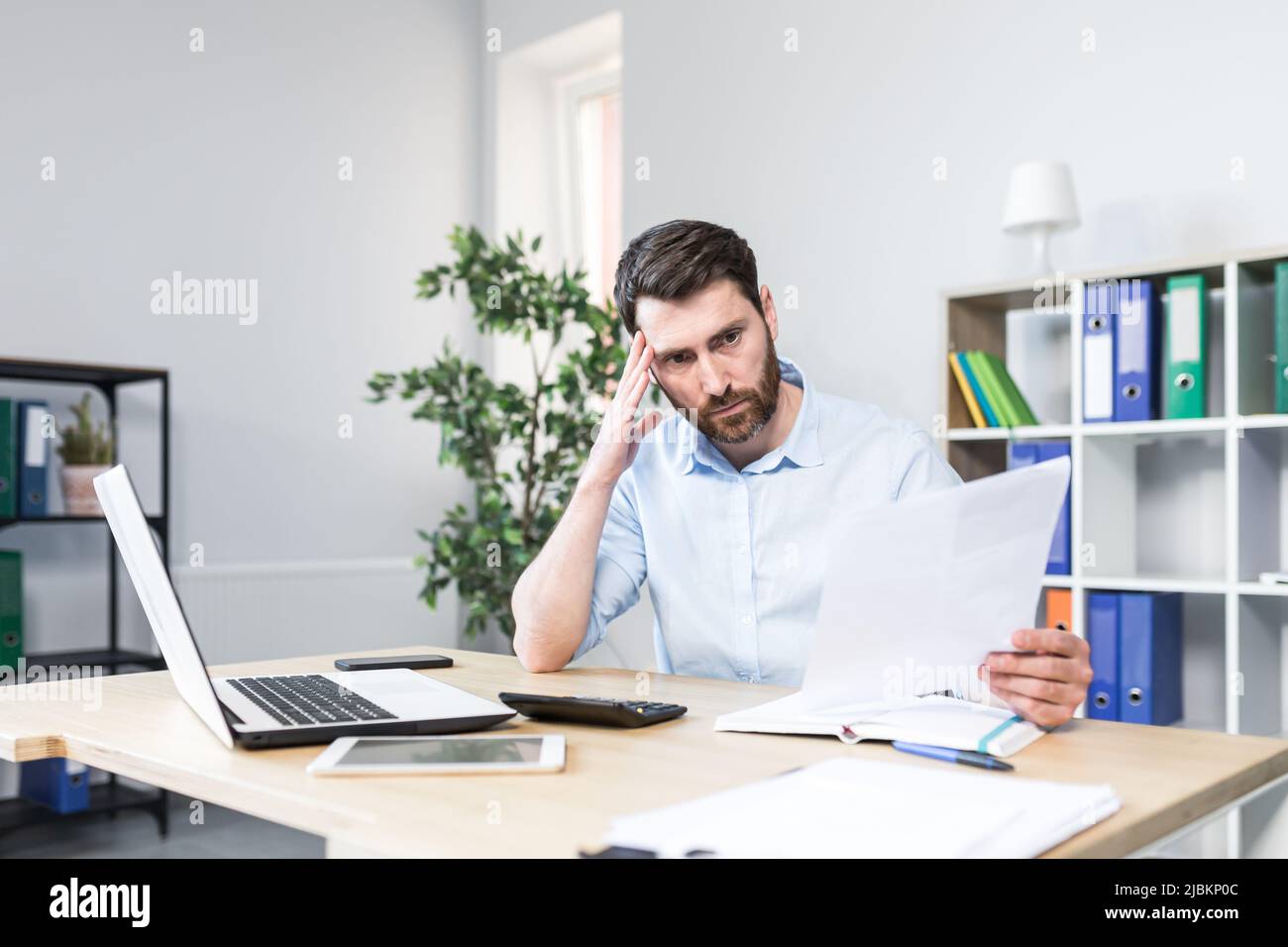 Un homme d'affaires frustré et inquiet regarde la mauvaise performance de l'entreprise sur les documents, un homme mal tient dans ses mains des rapports financiers avec err Banque D'Images