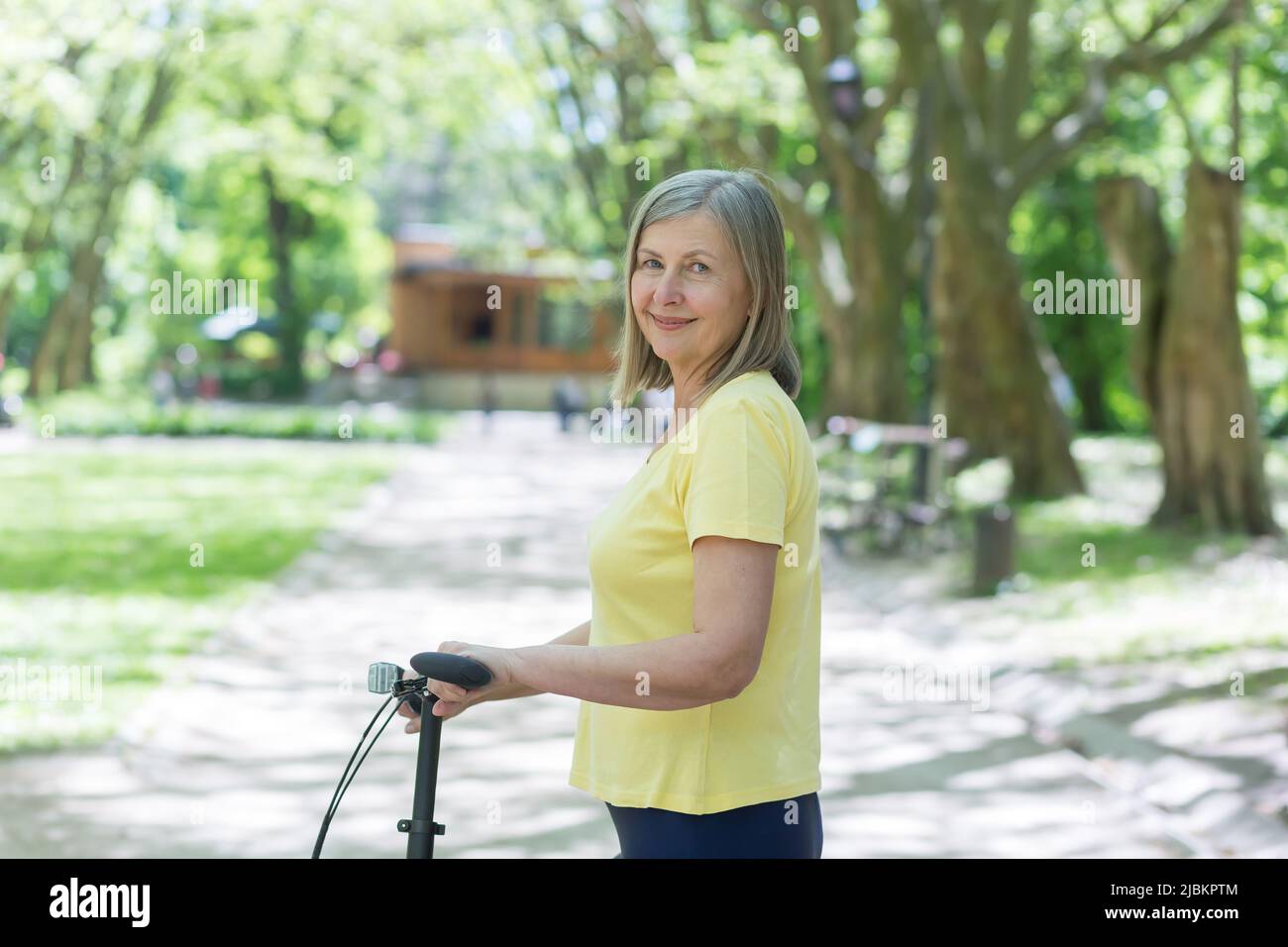 Portrait d'une femme active senior, d'une femme aux cheveux gris dans le parc, regardant l'appareil photo et souriant à vélo, jour d'été Banque D'Images