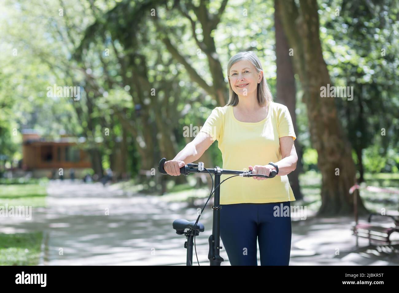 Portrait d'une femme active senior, d'une femme aux cheveux gris dans le parc, regardant l'appareil photo et souriant à vélo, jour d'été Banque D'Images