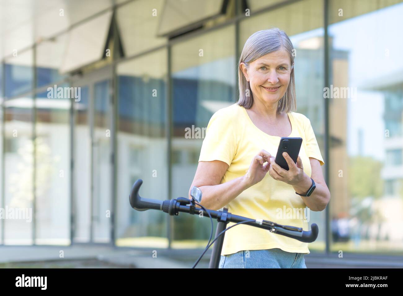 La femme âgée aux cheveux gris aime le téléphone lors d'une promenade estivale avec un vélo, pensionné souriant Banque D'Images