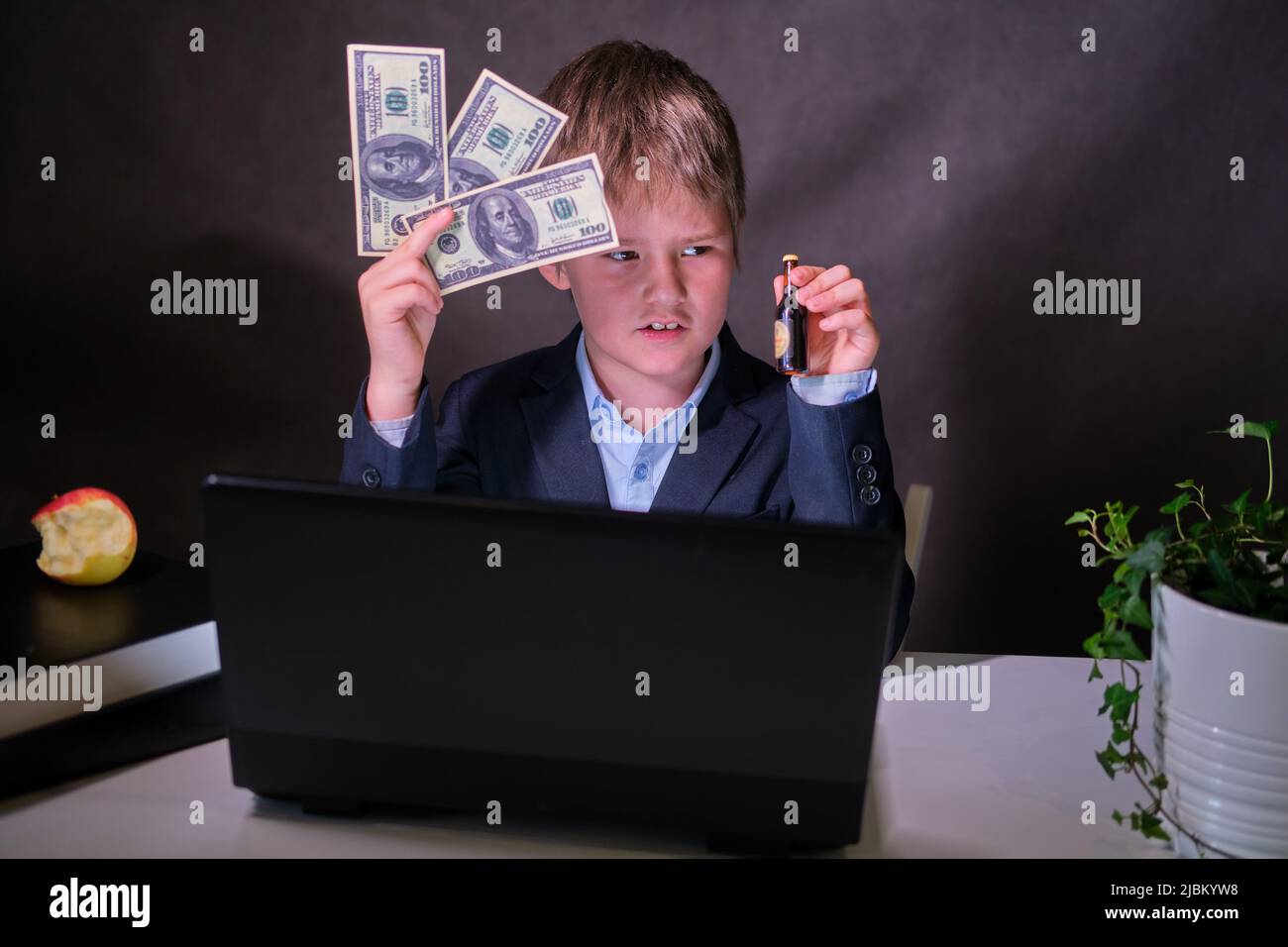 Un garçon heureux dans un costume d'école avec de l'argent et une bouteille d'alcool dans ses mains, copier l'espace sur un fond sombre de studio Banque D'Images