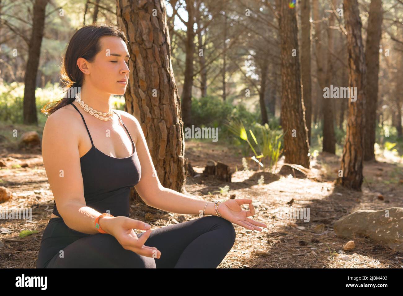 Belle jeune fille adulte en position lotus faisant du yoga au coucher du soleil dans une forêt entourée d'arbres. Gros plan, photo horizontale. Banque D'Images