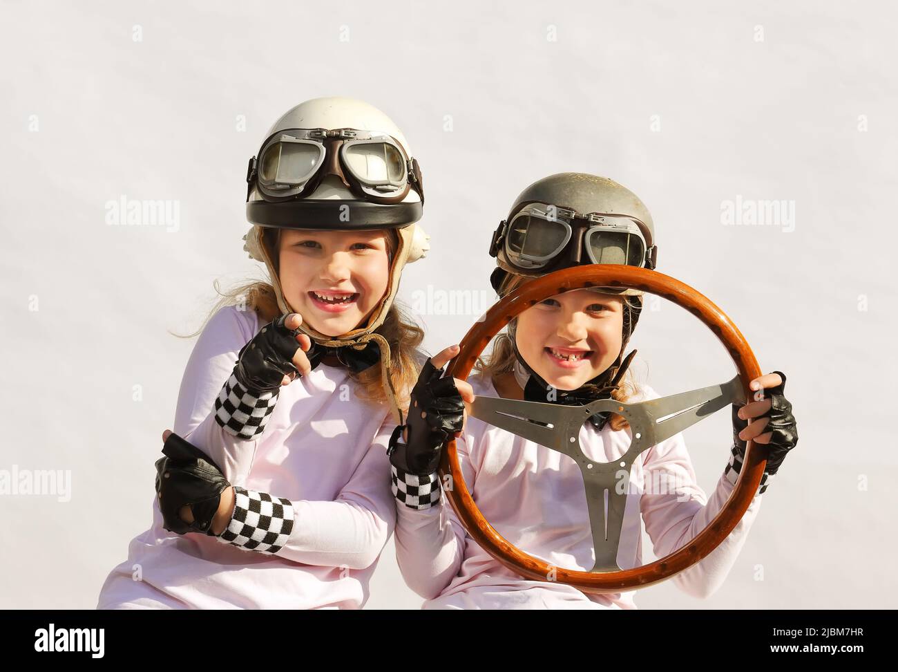 Les sœurs jumelles imaginent qu'elles conduisent une voiture de sport. Ils portent des casques vintage, des lunettes et utilisent un ancien volant en bois comme support. Banque D'Images
