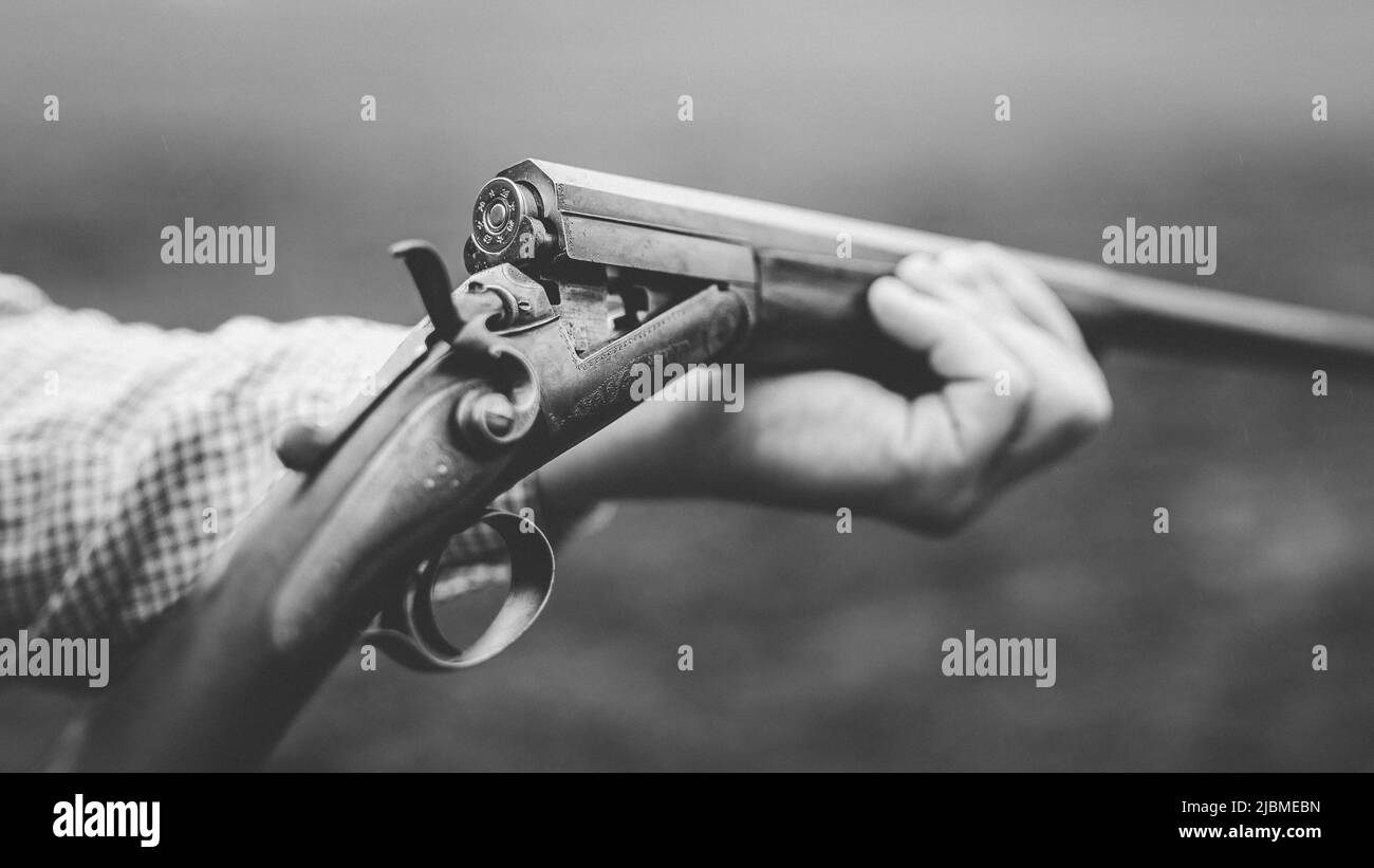 Gros plan du chasseur charge la cartouche sur le fusil en forêt, noir et blanc. Banque D'Images