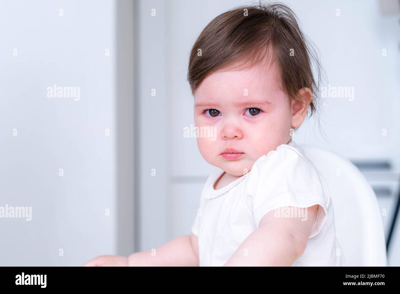 portrait malheureux pleurs bébé enfant assis sur une chaise haute sur la cuisine à la maison, bébé ne veut pas manger de la nourriture Banque D'Images