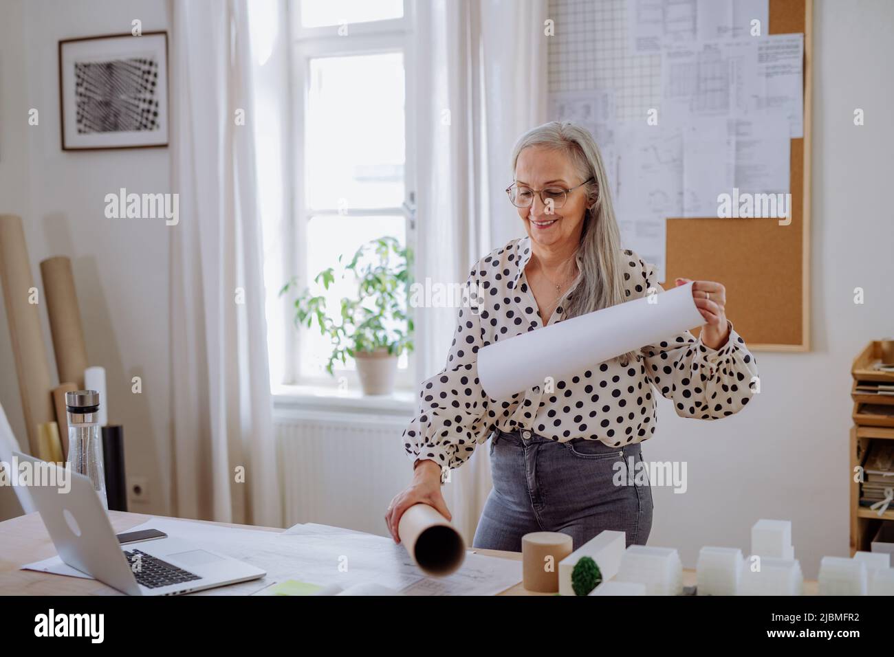 Femme architecte tirant des plans roulés hors du tube dans le bureau. Banque D'Images