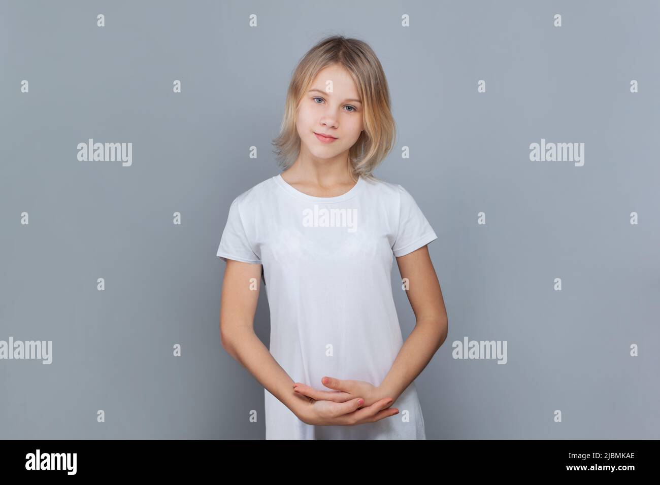 Jeune fille gaie de 10-12 ans posant contre un mur gris. Banque D'Images