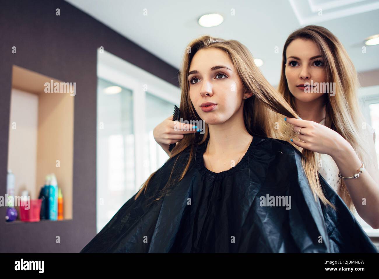 Coiffeur décidant avec la jeune cliente ce que la coupe de cheveux à faire dans le salon de coiffure. Deux belles blonds discutant d'une nouvelle coiffure Banque D'Images