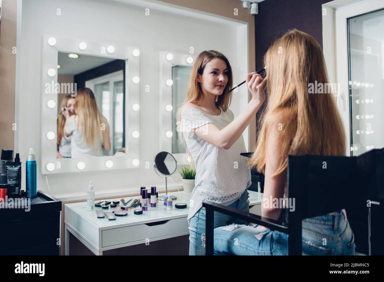 Esthéticienne caucasienne portant des vêtements décontractés engagés sur l'application de maquillage à la jeune femme cliente dans le magasin de beauté. Banque D'Images