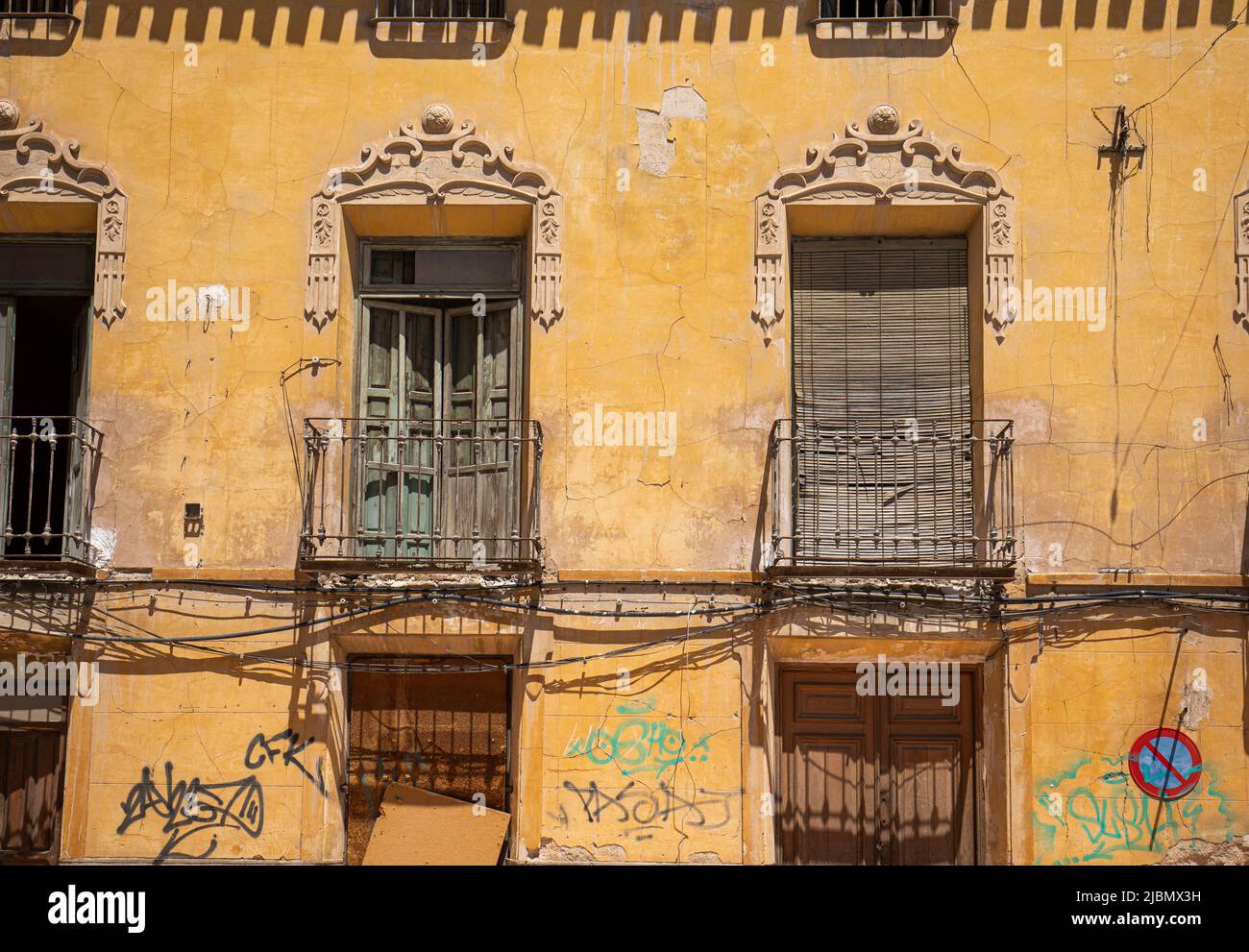 Façade d'un vieux bâtiment avec balcons et fenêtres très détériorées, avec graffiti et fissures sur la façade jaune Banque D'Images