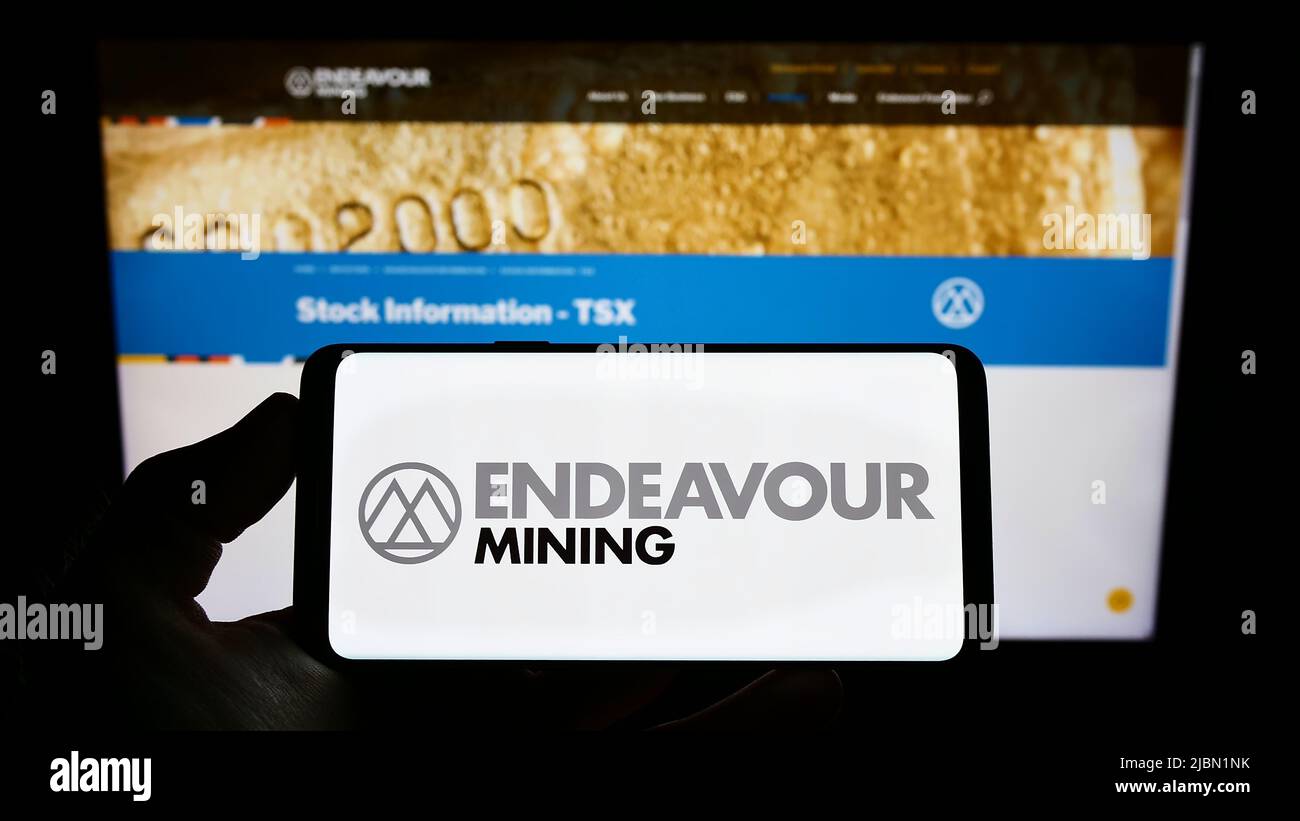 Personne tenant un téléphone portable avec le logo de la société d'exploration aurifère Endeavour Mining plc sur l'écran devant la page Web. Mise au point sur l'affichage du téléphone. Banque D'Images