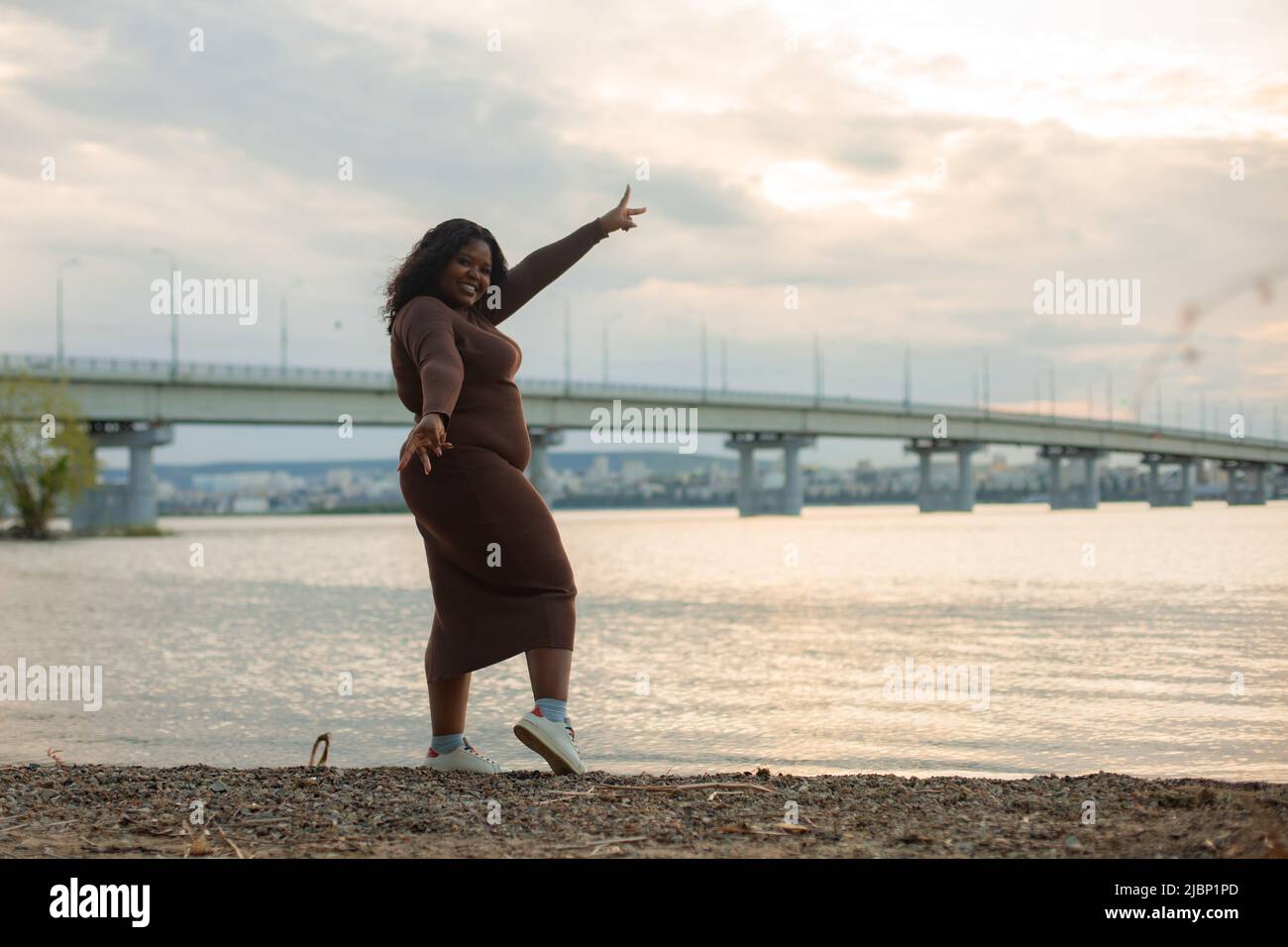 Curieusement souriante et ludique africaine afro-américaine plumeuse noire-cheveux multiculturel femme qui se berce autour de la plage de rivière Banque D'Images