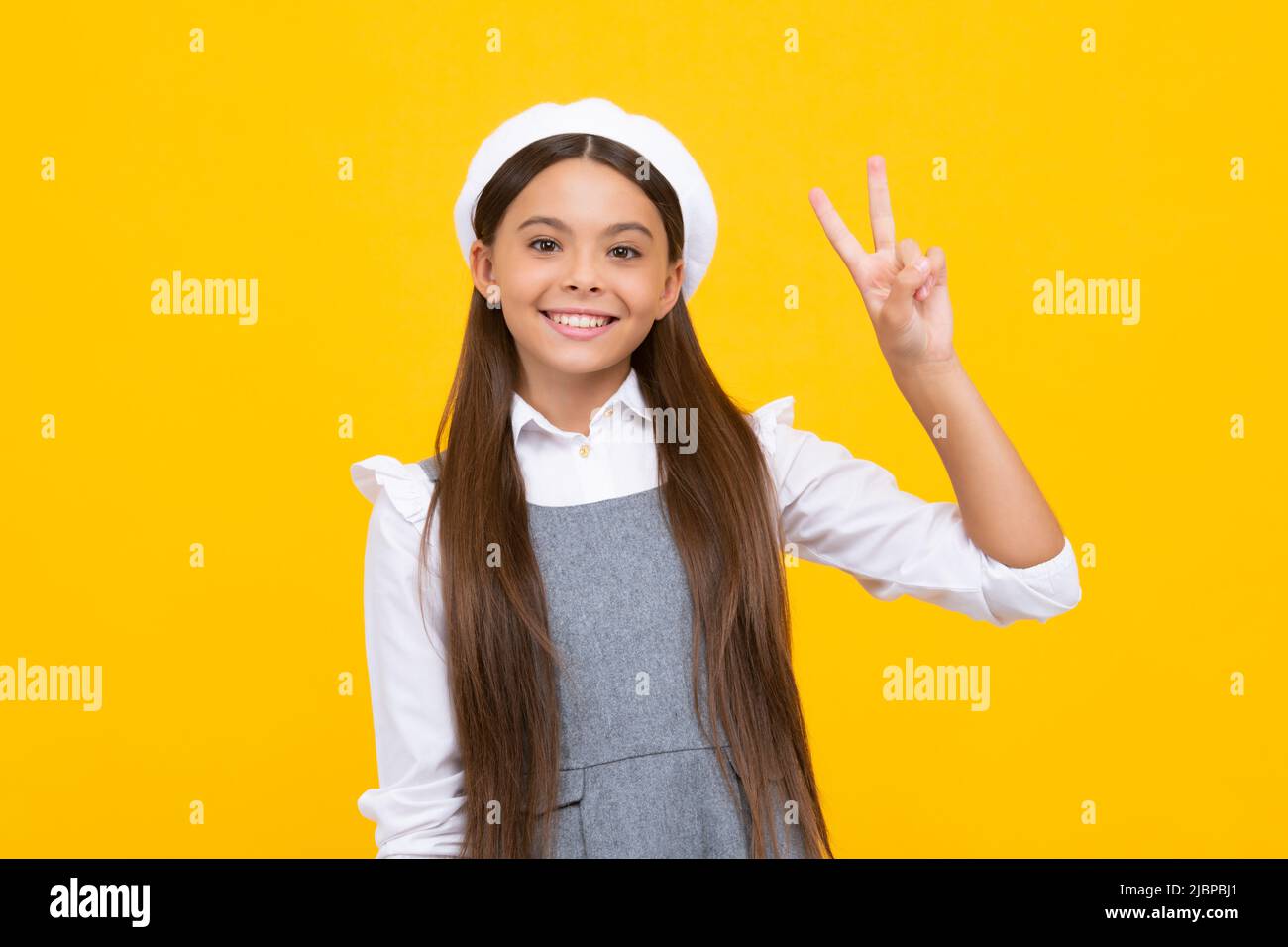 Adolescente fille debout sur un fond jaune isolé montrant les doigts faisant signe de victoire. Numéro deux, signe V. Bonne fille visage, positif et Banque D'Images