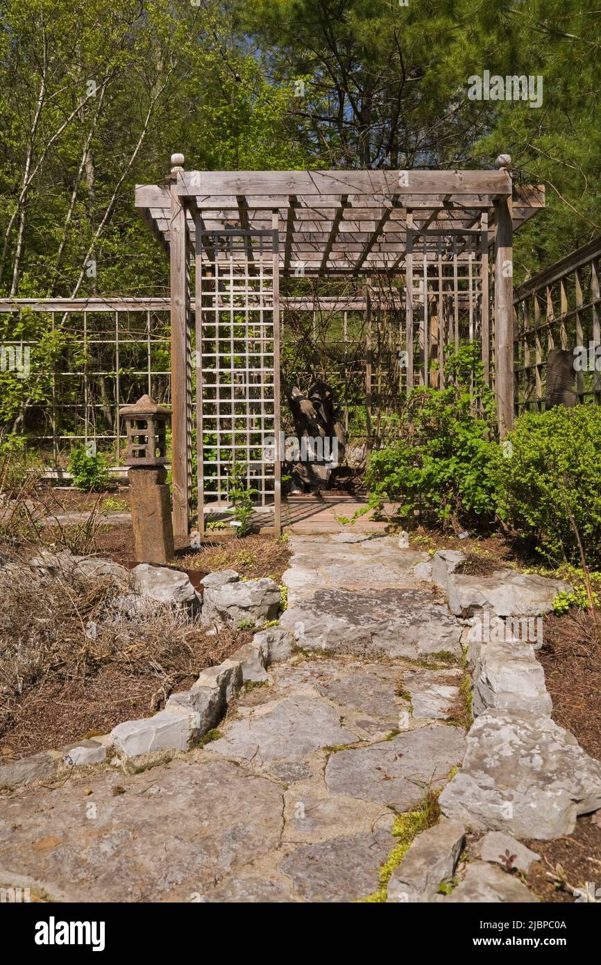 Chemin en pierre de drapeau menant à la pergola en bois de treillis dans le jardin paysagé de cour au printemps. Banque D'Images